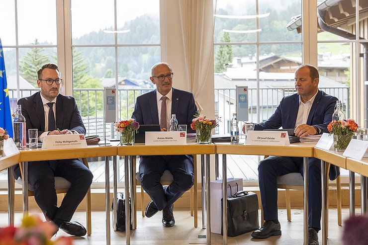 Drei Männer sitzen an einem Tisch und sprechen.