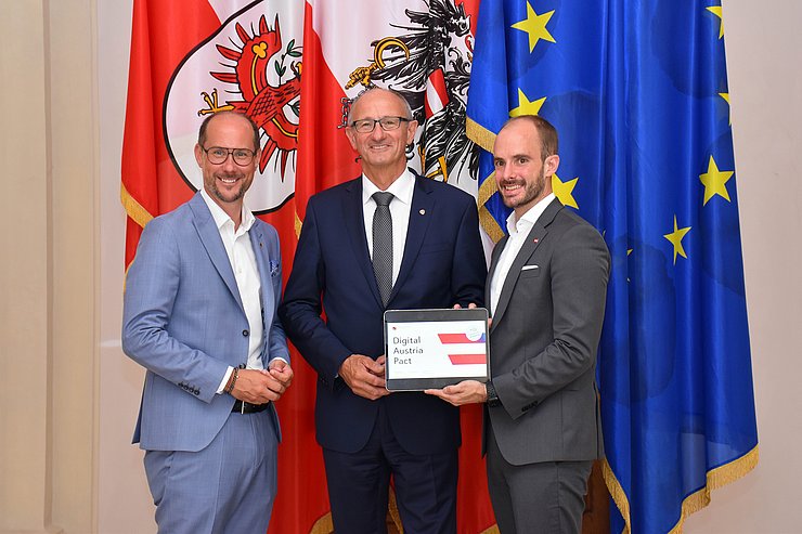 Landesrat Mario Gerber, Landeshauptmann Anton Mattle und Staatssekretär Florian Tursky stehen vor drei Fahnen und halten ein Tablet mit dem Schriftzug "Digital Austria Pact" in der Hand