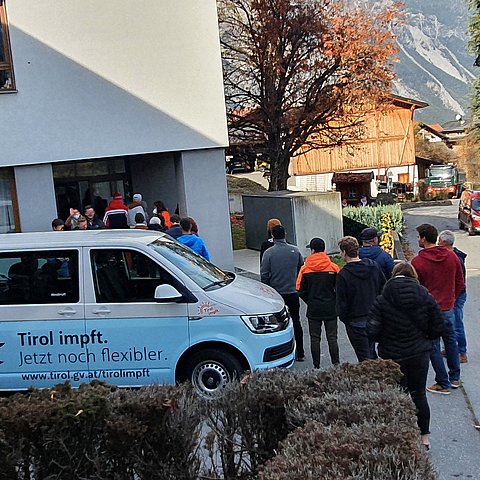 Eine Gruppe Menschen steht vor dem Gemeindeamt Schlange, davor steht auch der Impf-Van des Landes (mit Aufklebern)