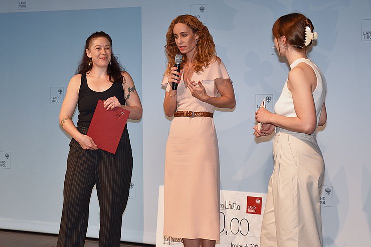 Lhotta, LRin Pawlata und Moderatorin am Podium - LRin hält Mikrophon in der Hand