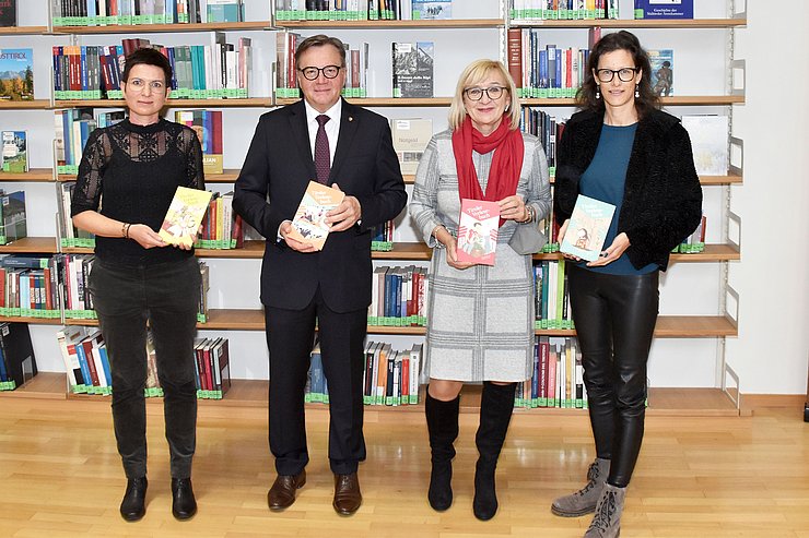 Autorin Carolina Schutti, Landeshauptmann Günther Platter, Bildungslandesrätin Beate Palfrader und Fachgruppenobfrau der Buch- und Medienwirtschaft Tirol Sonja Altenburger vor einer Bücherwand mit den 4 Tiroler Vorlesebüchern in Händen