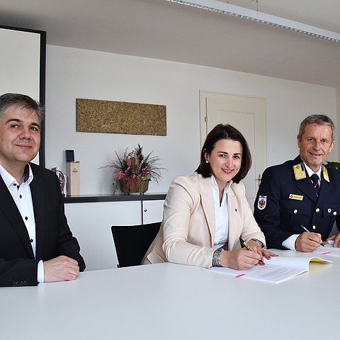 LRin Mair und Stock am Tisch sitzend Vertrag unterschreibend, daneben Reister sitzend