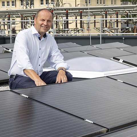 LHStv Josef Geisler kniet vor einer PV-Anlage.