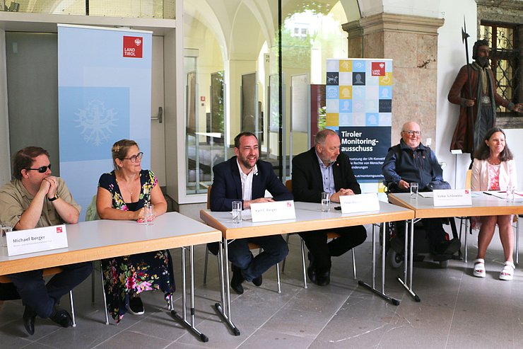 Tisch mit RednerInnen, im Hintergrund 2 Roll-ups des Landes/Monitoringausschusses