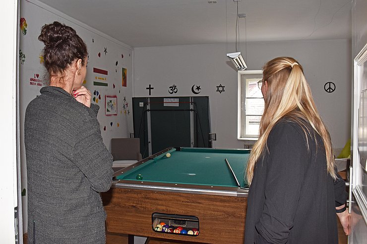 LRin und Haider blicken in Raum mit Billardtisch und Aufklebern an den Wänden