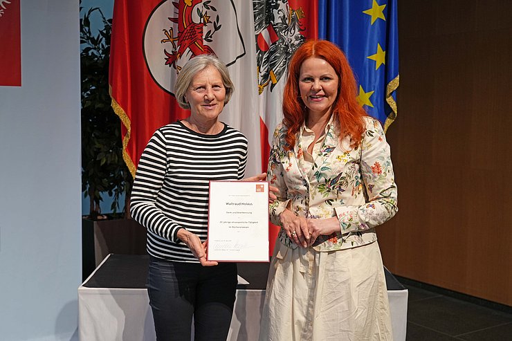 © Land Tirol/Reiter Zwei Menschen posieren vor Flaggen.