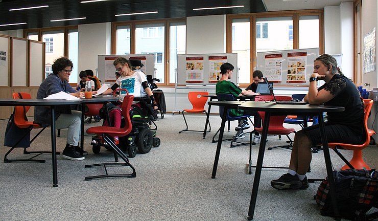 Raum mit Jugendlichen, die an Tischen sitzen