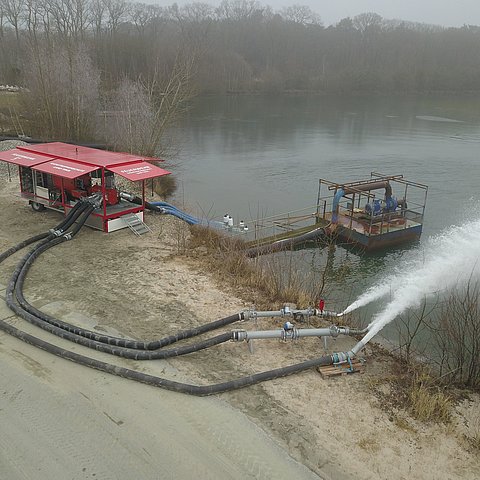 Pumpe neben See stehend. Wasser spritzt aus Rohren