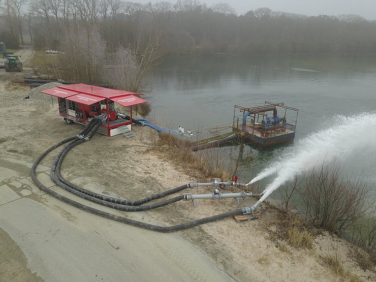 Pumpe neben See stehend. Wasser spritzt aus Rohren