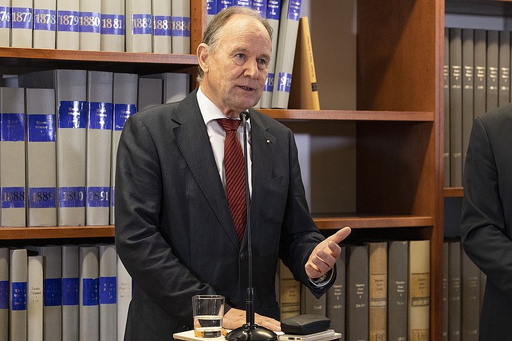 © Land Tirol/Die Fotografen Vereinsobmann des Vereins "Tiroler Landesmuseum Ferdinandeum" Franz Pegger steht hinter einem Rednerpult und vor einem Bücherregal