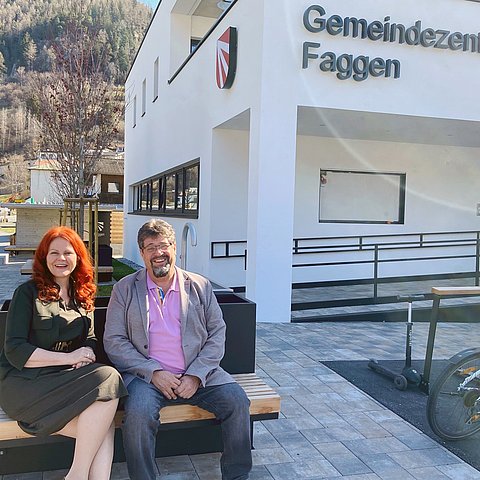 Eine Frau und ein Mann sitzen vor einem Haus.