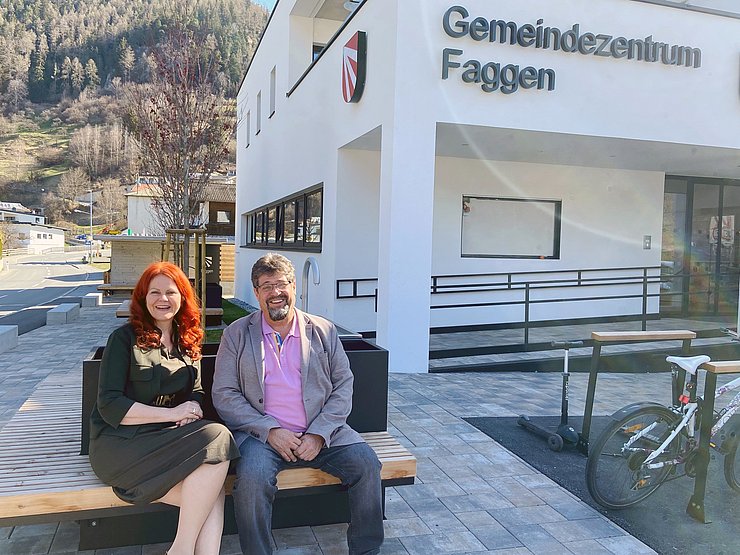 Eine Frau und ein Mann sitzen vor einem Haus.