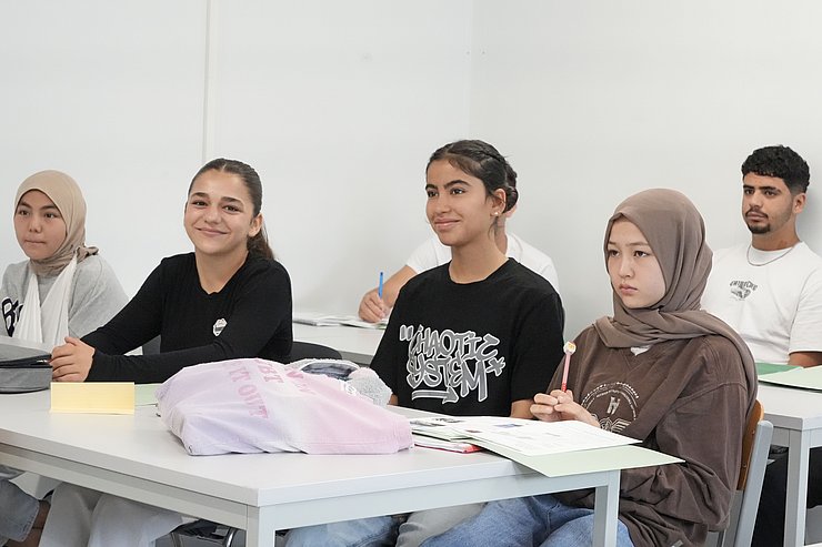 Mehrere Schülerinnen und Schüler sitzen in einer Klasse.