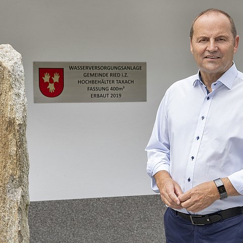 Bild von LHStv Josef Geisler vor einem Gebäude. Im Hintergrund ist ein Schild zu sehen, auf welchem Wasserversorgungsanlage Gemeinde Ried i. Z. zu lesen ist