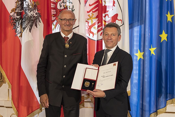 © Land Tirol/Die Fotografen links LH Mattle, Rechts Herr Meindl, hält Urkunde und Orden