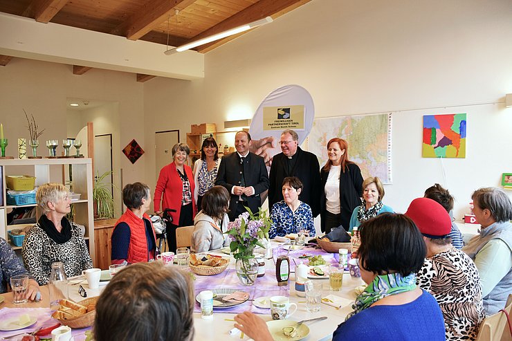 Personen um Tisch versammelt, stehend die namentlich angeführten Personen