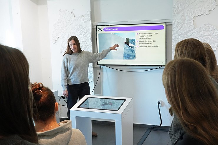 Frau vor Fernseher redend und erklärend, SchülerInnen hören zu