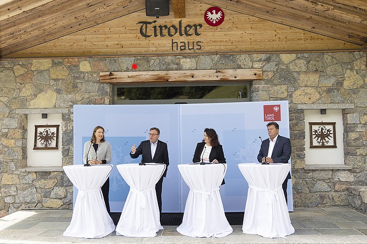 © Land Tirol/Die Fotografen LRin Leja, LH Platter, LHStvin Felipe und Gemeideverbandpräsident Schöpf jeweils an einem Rednerpult vor dem Tiroler Haus