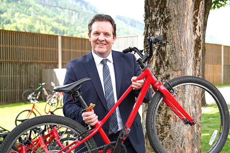 Zumtobel hält rotes Kinderfahrrad in die Luft