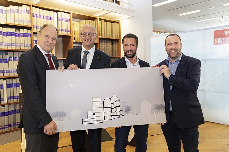 © Land Tirol/Die Fotografen Von links: Vereinsobmann Franz Pegger, LH Anton Mattle, Hochbaureferent LHStv Georg Dornauer und Ferdinandeums-Direktor Karl C. Berger stehen mit einem Bild des neuen Ferdinandeums vor einem Bücherregal