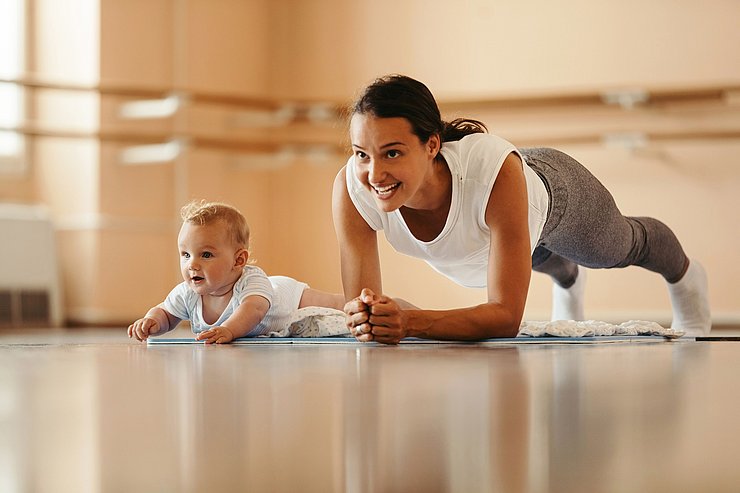 © Shutterstock Junge Frau in Plank-Position, neben ihr ein Baby