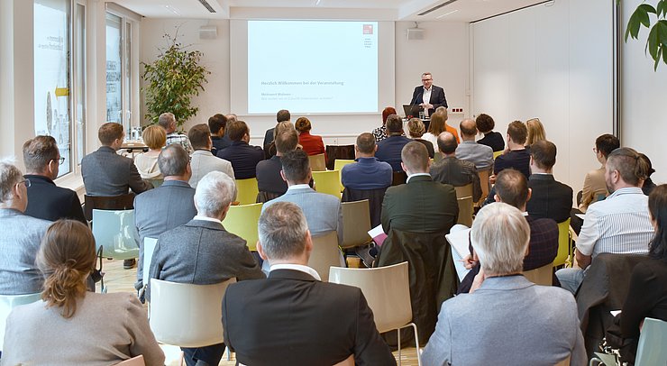 © Land Tirol/Pölzl Publikum auf Stüheln sitzend lauscht dem Vortrag von LR Tratter, der im Hintergrund steht