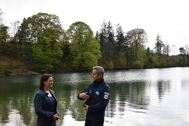 © Land Tirol/Pölzl Mair (links) und Stock stehend und miteinander redend. Im Hintergrund das türkise Wasser des Reintalersee. Der Himmel ist wolkenverhangen