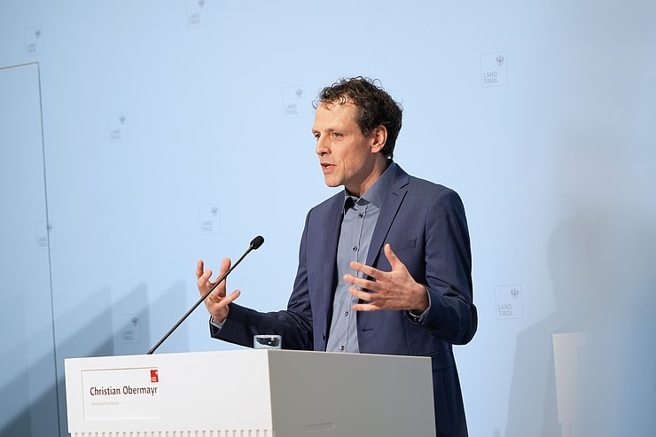 © Land Tirol/Neuner Ein Mann steht an einem Rednerpult und hebt dabei beide Hände.