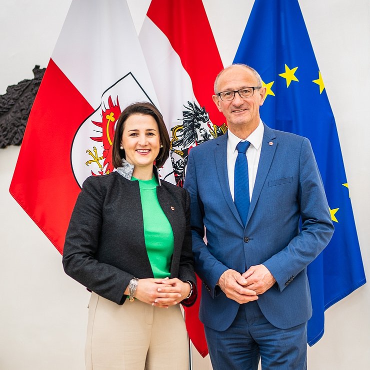LH Mattle steht neben LRin Mair in seinem Büro im Landhaus - vor einer Tirol-, Österreich- und Europafahne.