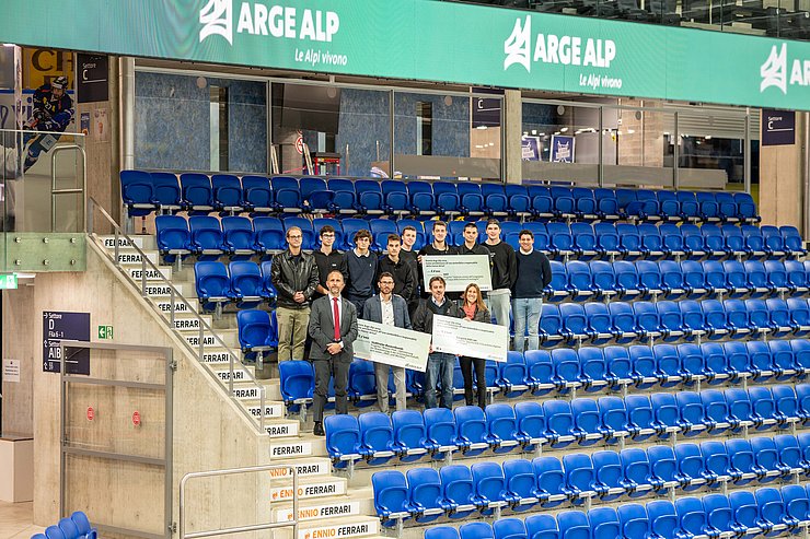 © Kanton Tessin Personen stehen mit großem Gutschein bei Stühlen in Eishockeyhalle
