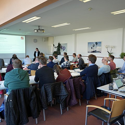 Kursraum mit Menschen an Tischen sitzend; Landesrätin Mair vor der Gruppe stehend und sprechend