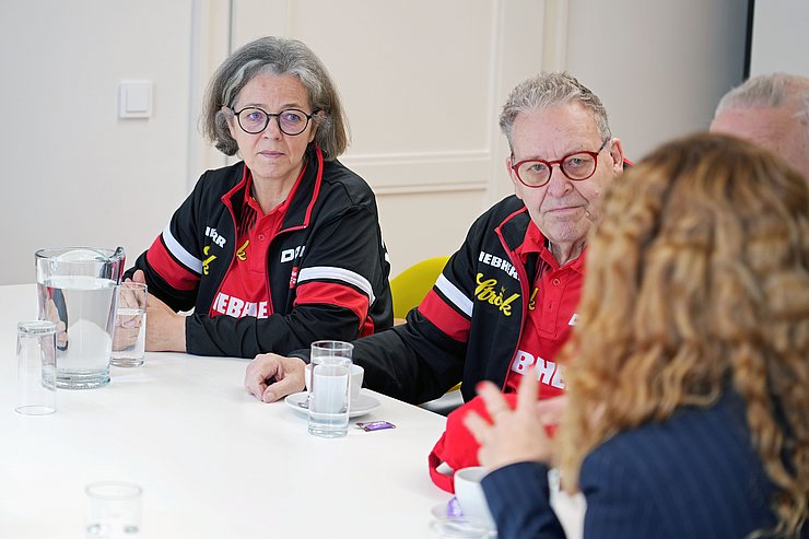 Der Tisch wird aus einem anderen Blickwinkel gezeigt, eine Frau und ein Mann schauen in Richtung der Landesrätin. 