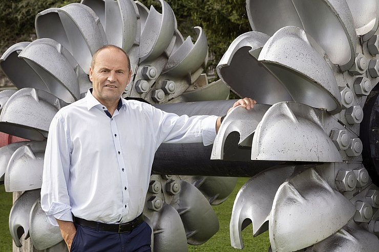 Landeshauptmann-Stellvertreter Geisler an einer Turbine angelehnt. Hinter ihm befindet sich eine weitere Turbine.