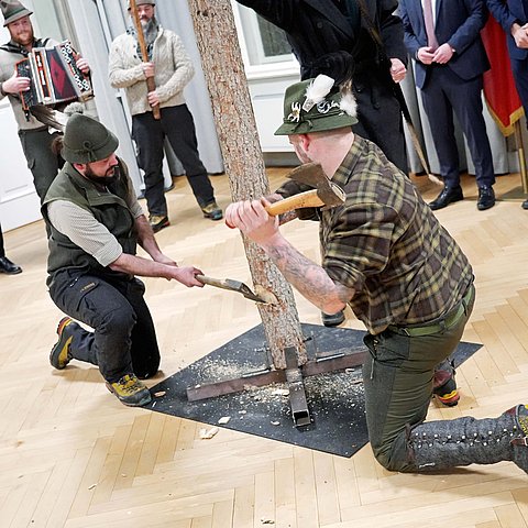 Zwei Mitglieder der Larchzieher arbeiten auf dem Baumstamm mit Äxten ein.