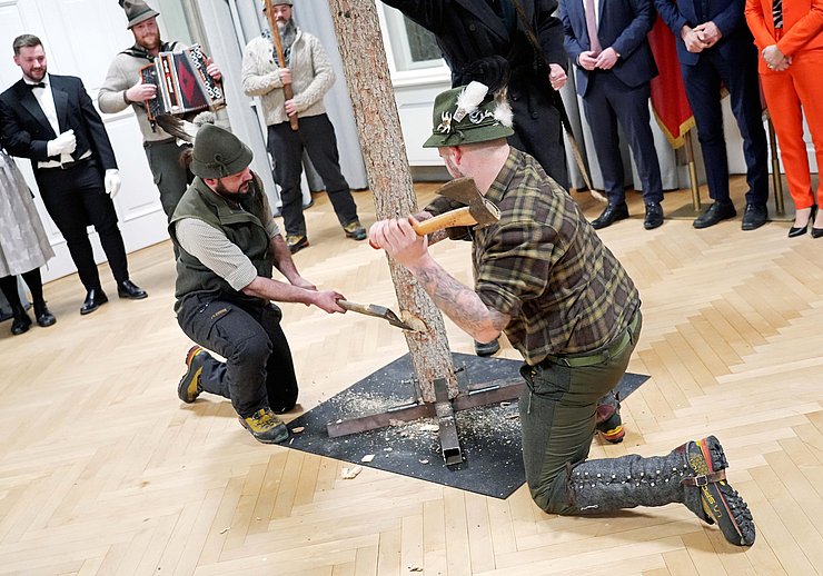 Zwei Mitglieder der Larchzieher arbeiten auf dem Baumstamm mit Äxten ein.