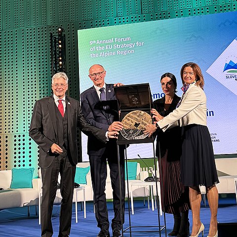 zwei Männer und zwei Frauen auf Bühne stehend mit symbolischen Rad in der mitte