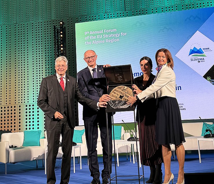 zwei Männer und zwei Frauen auf Bühne stehend mit symbolischen Rad in der mitte