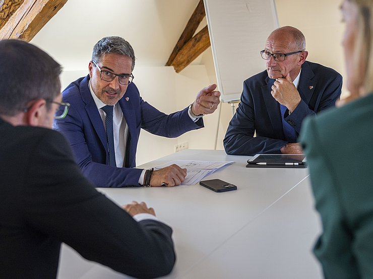 LH Anton Mattle, LH Arno Kompatscher und LH Maurizio Fugatti sitzen an einem Tisch und sprechen miteinander.