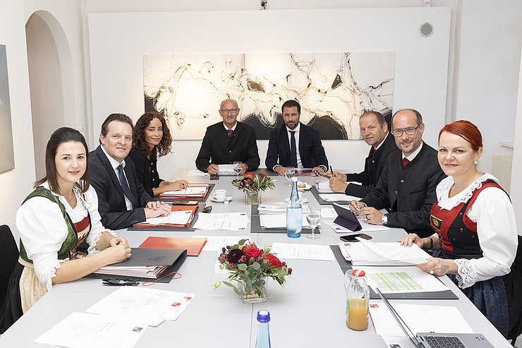 © Land Tirol/Die Fotografen Regierungsmitglieder sitzen um Runden Tisch - schauen in Kamera