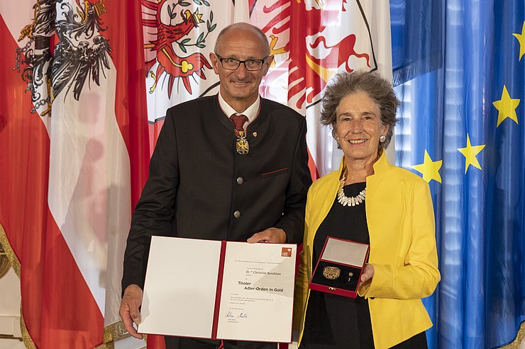 © Land Tirol/Die Fotografen links LH Mattle, rechts Frau Bandtlow, halten gemeinsam Urkunde und Orden
