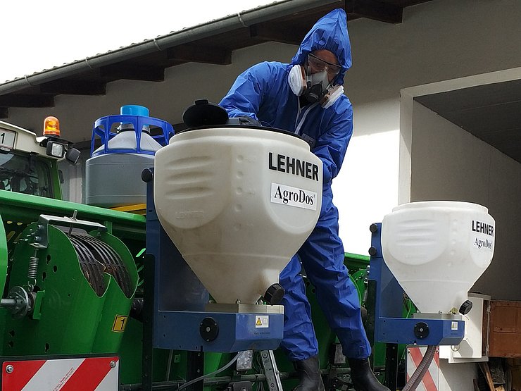 © Land Tirol eine Person in Schutzkleidung befüllt einen Granulatstreuer, welcher an einem Traktor montiert ist