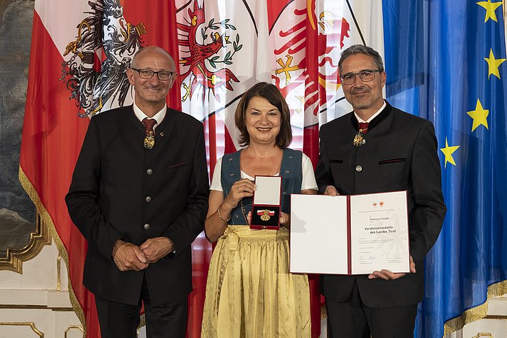 © Land Tirol/Die Fotografen links LH Mattle, in der Mitte Frau Handle und rechts LH Kompatscher, halten Medaille und Verdiensturkunde