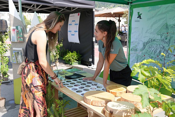 Frau hinter Infostand erklärt anderer Frau etwas