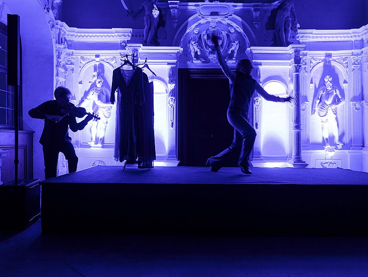 © LPA/Tiberio Sorvillo Ein Mann spielt Geige, ein anderer tanzt, alles ist in blaues Licht getaucht.