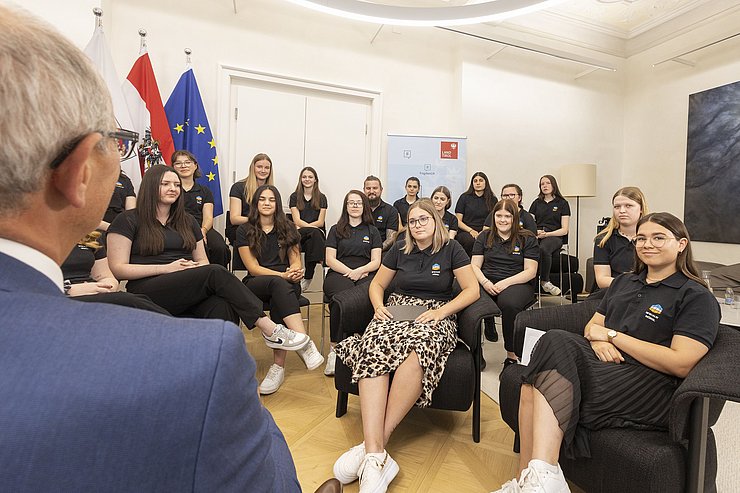 © Land Tirol/Die Fotografen Die zwei Schülerinnen Leonie Bangheri und Valentina Madreiter sitzen vor LH Mattle und stellen ihm die ausgearbeiteten Fragen.