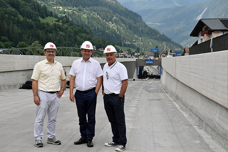 Der Leiter des Baubezirksamts Imst Bernd Stigger steht links neben Landeshauptmann-Stellvertreter Josef Geisler. Rechts neben dem Landeshauptmann-Stellvertreter steht Bürgermeister Heinz Kofler. Die drei Männer stehen vor der Baustelle der Unterführung.