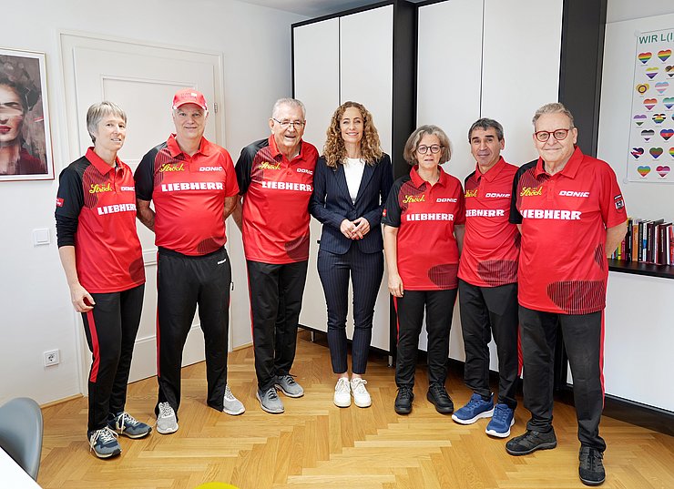 Die Männer und Frauen stehen in ihren roten Trikots neben Landesrätin Eva Pawlata.