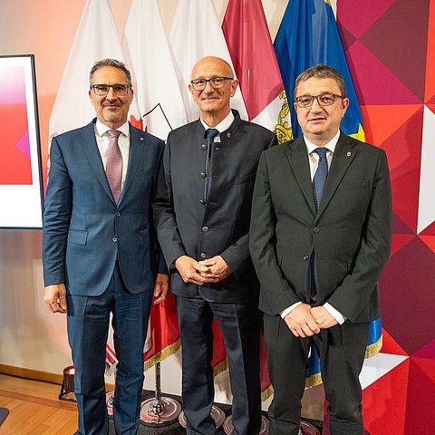 LHs stehen nebeneinander vor Fahnen