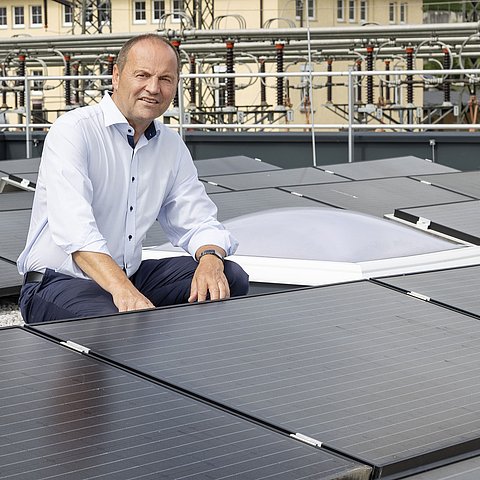 LHStv Geisler kniet zwischen PV-Paneelen auf Dach eines Gebäudes