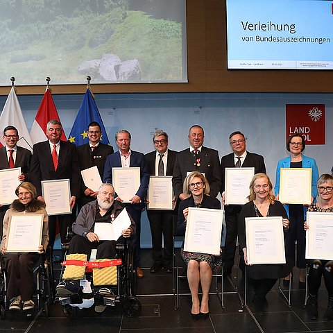 Im Landhaus sitzen bzw. stehen 13 Personen, die Urkunden zu ihrer Bundesauszeichnung in Händen halten.